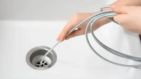 Hands feeding a drain cable into the drain of a white sink