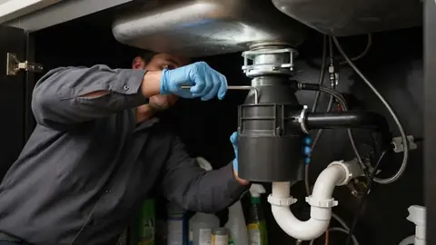 Plumber servicing a garbage disposal under a kitchen sink