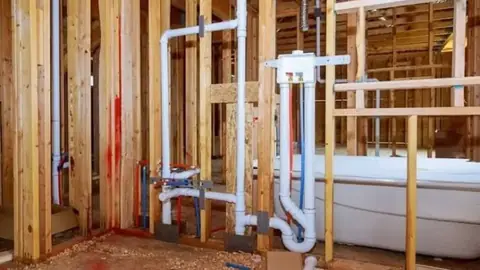 Bathroom wall framing with new drain and vent pipes and a bathtub in place during rough-in